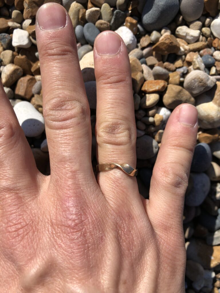 brass möbius ring worn on a hand that rests on a background of beach pebbles